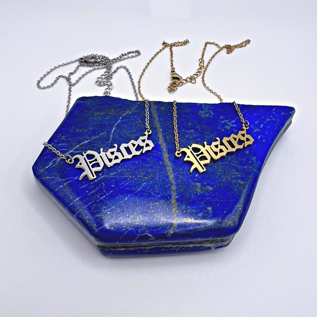 Displayed on a large, textured blue rock with white and gold veins, two Zodiac Necklaces from Ascention Beauty capture the cosmic essence of their Pisces pendants. With one pendant shimmering in silver and the other in gold, their metallic chains offer a striking contrast to the rock's natural beauty.