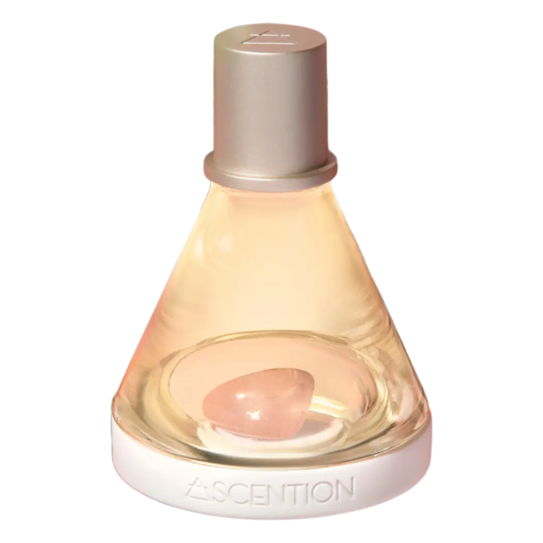 The Ascent To Love With Rose Quartz Crystal from ASCENTION BEAUTY CO is a conical glass bottle designed for wellness fragrance. It contains a rose quartz stone, symbolizing self-love, and features a white base labeled Ascension. The bottle has a sleek and modern appearance with its metallic cap.